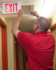 Man Accessing Emergency Exit battery with a screwdriver